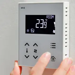 Dłoń dostosowuje **ekonomiczne ustawienie pompy ciepła** na termostacie. Wyświetlacz pokazuje 23.9°C.