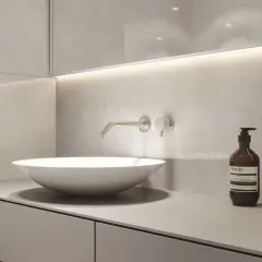Nowoczesny blat do łazienki z umywalką nablatową i baterią ścienną. Minimalistyczny design, szare płytki i dyskretne oświetlenie.