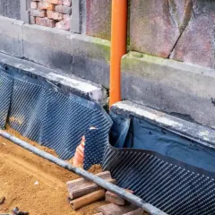 Ocieplenie fundamentów w starym domu: folia kubełkowa i rura odpływowa chronią ściany przed wilgocią.