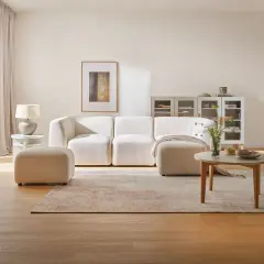 Jasny salon: biel, szary i drewno. Miękka sofa, puf, stolik kawowy i dywan tworzą przytulną przestrzeń.