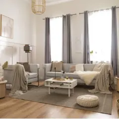 Elegancki styl boho wnętrza: jasna kanapa, fotel, stolik kawowy, dywan, pleciony kosz i dekoracje tworzą przytulną atmosferę.