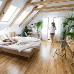 Przytulne aranżacje łóżka w sypialni na poddaszu. Mężczyzna śpi, kobieta budzi się przy oknie.