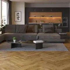 Nowoczesny salon z szarą sofą i ciemną podłogą. W tle kuchnia z drewnianymi frontami i oświetleniem.