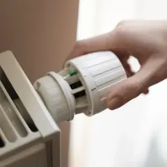 Ręka reguluje termostat grzejnika. Od kiedy zakaz ogrzewania gazem, oszczędzamy ciepło.