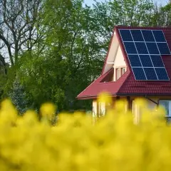 Dom z panelami fotowoltaicznymi na dachu, otoczony kwitnącym rzepakiem. Rozbudowa instalacji fotowoltaicznej w malowniczym otoczeniu.