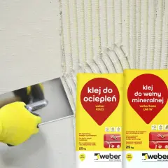 Gąbkowanie kleju na elewacji. Ręka w żółtej rękawicy rozprowadza klej na izolacji, obok worki z klejem do ociepleń.