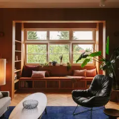 Przytulny salon w stylu mid century z wygodną kanapą przy oknie, fotelem i drewnianymi meblami.
