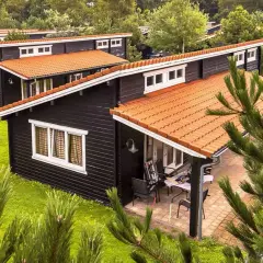 Czarny bungalow z pomarańczowym dachem, otoczony zielenią. Idealne miejsce na wakacje, czyż nie?