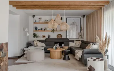 Przytulny salon w stylu boho z szarą sofą, plecionymi lampami i drewnianymi belkami.