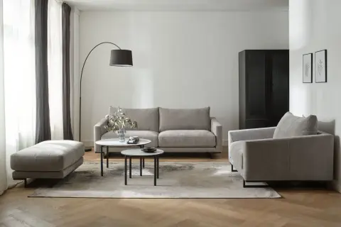 Nowoczesny salon z dwiema sofami, fotelem i pufą. W centrum dwie niskie stoliki kawowe.