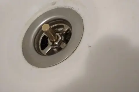 Metalowy korek do wanny z pokrętłem, widoczny mechanizm i włosy. Potrzebna naprawa.