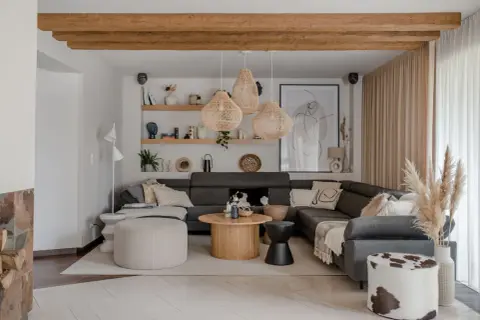 Przytulny salon w stylu boho z szarą sofą, plecionymi lampami i drewnianymi belkami.