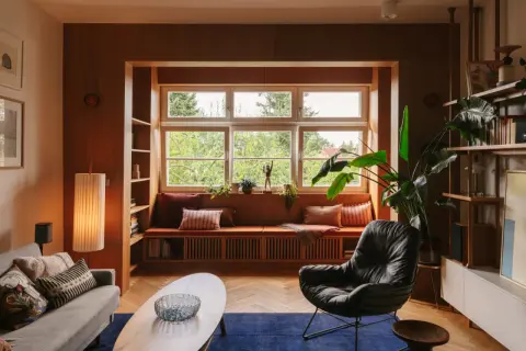 Przytulny salon w stylu mid century z wygodną kanapą przy oknie, fotelem i drewnianymi meblami.
