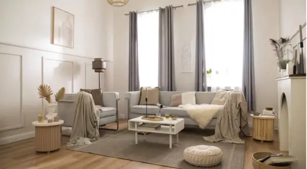 Elegancki styl boho wnętrza: jasna kanapa, fotel, stolik kawowy, dywan, pleciony kosz i dekoracje tworzą przytulną atmosferę.