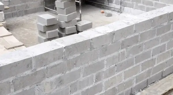 Budowa muru z szarego bloczka betonowego. Widać stosy bloczków, przygotowane do murowania.