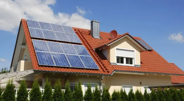 Dach domu pokryty czerwonymi dachówkami, na którym zamontowano panele fotowoltaiczne. Widać różne rodzaje paneli fotowoltaicznych, które zbierają energię słoneczną.
