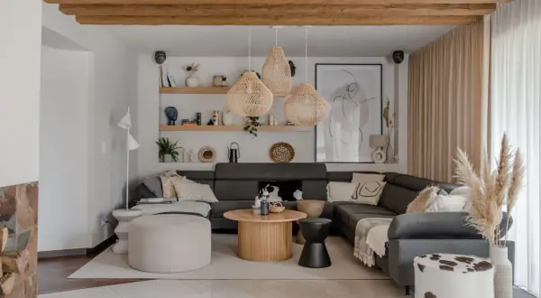 Przytulny salon w stylu boho z szarą sofą, plecionymi lampami i drewnianymi belkami.