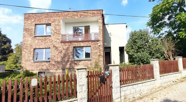 Dom kostka prl z cegły, z balkonem i drewnianym płotem.