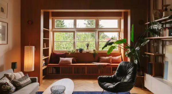 Przytulny salon w stylu mid century z wygodną kanapą przy oknie, fotelem i drewnianymi meblami.