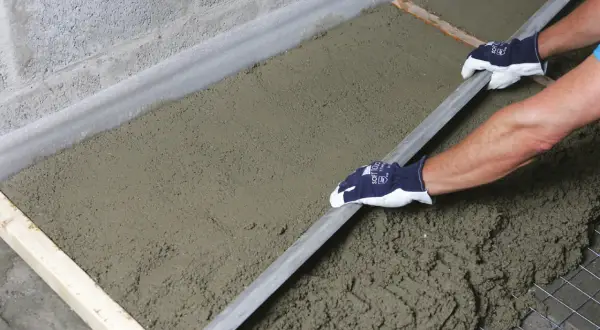 Ręce w rękawiczkach wygładzają świeży beton, który leży na siatce zbrojeniowej i styropianie. To praca przy budowie, gdzie styrobeton czy styropian odgrywają kluczową rolę.