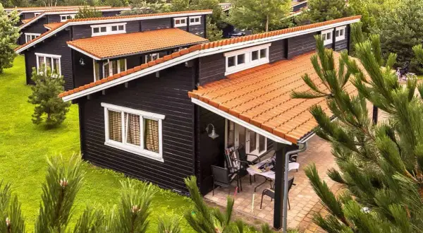Czarny bungalow z pomarańczowym dachem, otoczony zielenią. Idealne miejsce na wakacje, czyż nie?