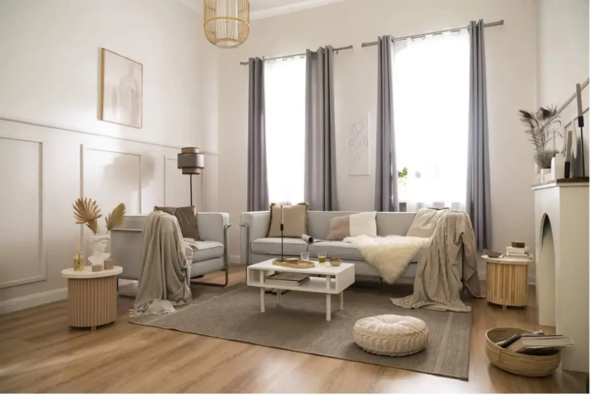 Elegancki styl boho wnętrza: jasna kanapa, fotel, stolik kawowy, dywan, pleciony kosz i dekoracje tworzą przytulną atmosferę.