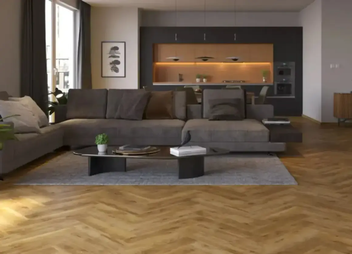 Nowoczesny salon z szarą sofą i ciemną podłogą. W tle kuchnia z drewnianymi frontami i oświetleniem.