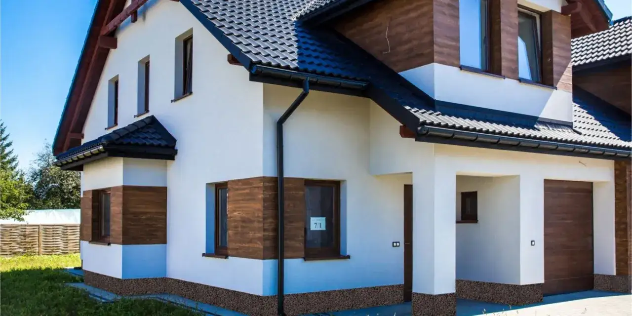 Nowy dom z białym tynkiem, drewnianymi elementami i ozdobnym cok&oacute;ł wok&oacute;ł domu.