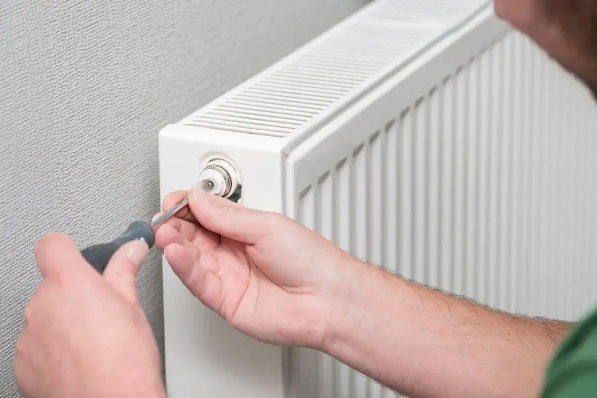 Ręka z wkrętakiem odpowietrza grzejnik. Zastanawiasz się, od kt&oacute;rego grzejnika zacząć odpowietrzanie? Zacznij od tego najbliżej kotła.