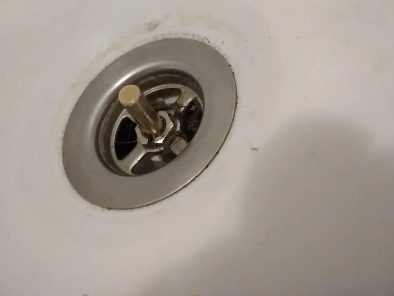Metalowy korek do wanny z pokrętłem, widoczny mechanizm i włosy. Potrzebna naprawa.