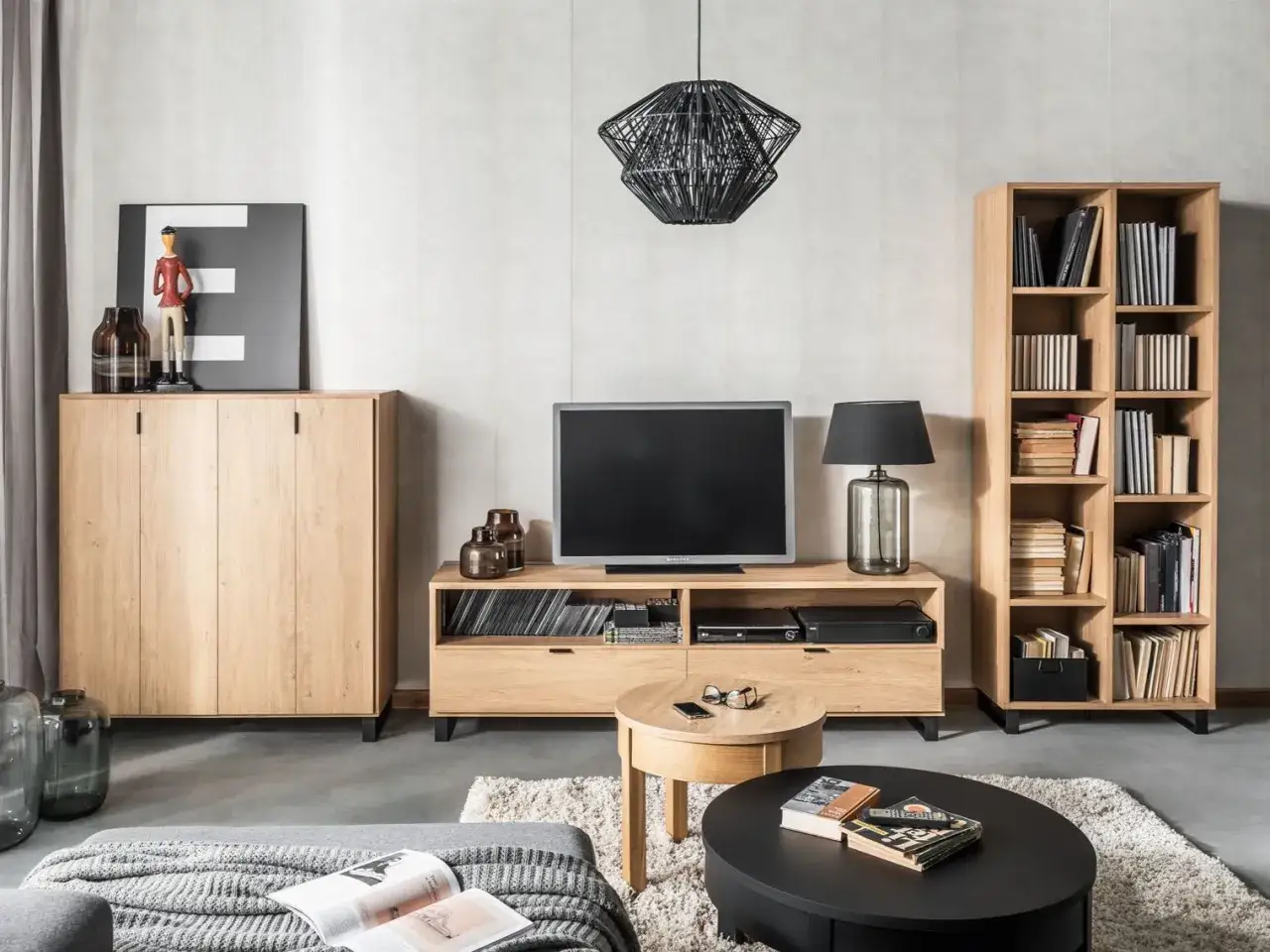 Nowoczesny salon z ciemną podłogą, drewnianymi meblami, telewizorem i regałem pełnym książek.