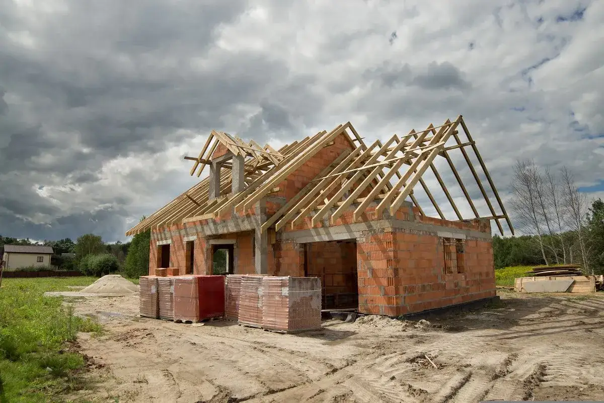 Budowa domu jednorodzinnego w toku. Dom z cegły, z widoczną konstrukcją dachu. Materiały budowlane na placu.
