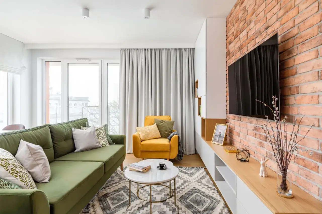 Zielona sofa i ż&oacute;łty fotel w salonie z ceglaną ścianą. Czy to sofa czy kanapa? Zależy od wielkości i przeznaczenia.