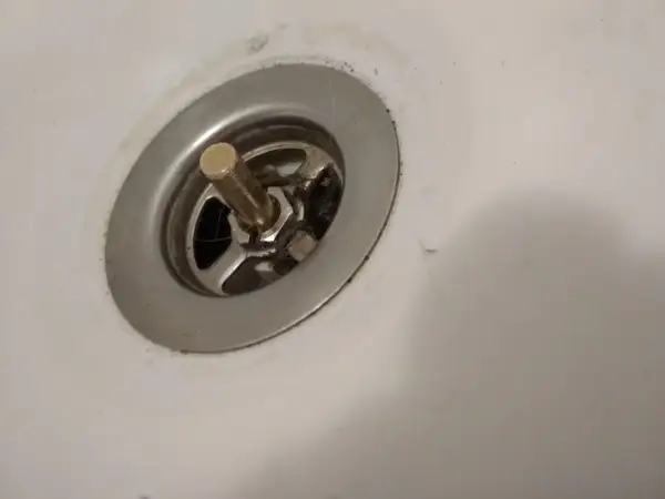 Metalowy korek do wanny z pokrętłem, widoczny mechanizm i włosy. Potrzebna naprawa.