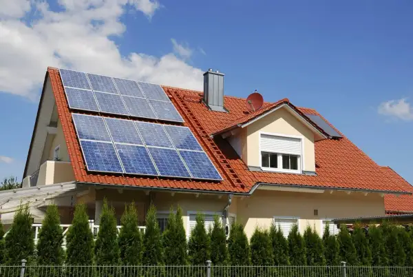 Dach domu pokryty czerwonymi dachówkami, na którym zamontowano panele fotowoltaiczne. Widać różne rodzaje paneli fotowoltaicznych, które zbierają energię słoneczną.