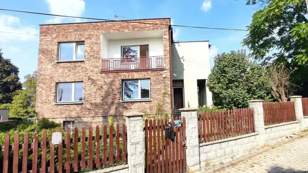 Dom kostka prl z cegły, z balkonem i drewnianym płotem.